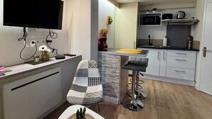 A compact kitchen with a flat-screen TV, a bar stool, and a small table with a cactus. - Casa Cloutiers #1 -Studio RDC -Hyper Centre Brive (Brive-la-Gaillarde)