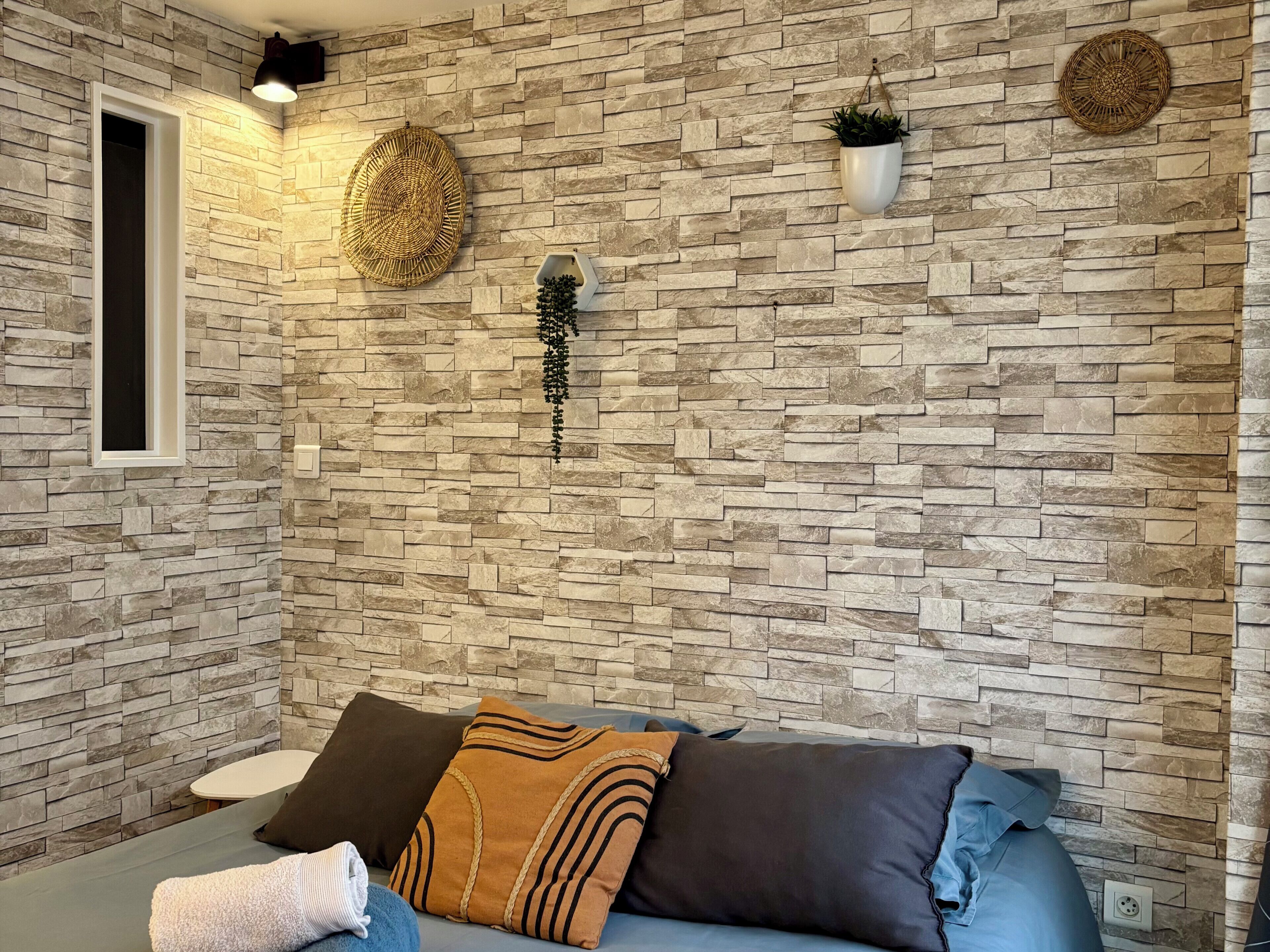 Une salle de spa avec un mur en pierre, une table de massage et une petite fenêtre.