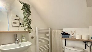 A small, clean bathroom with a white sink, mirror, and toilet. There is a white towel rack, a plant hanging above the sink, and a shelf with toiletries. - Casa Cloutiers #1 -Studio RDC -Hyper Centre Brive (Brive-la-Gaillarde)