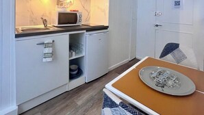 A compact kitchen with white cabinetry, a microwave, a sink, and a small refrigerator. There is a door with a QR code and a mirror on the wall. - Casa Cloutiers #2 - Studio - Hyper Centre Brive (Brive-la-Gaillarde)