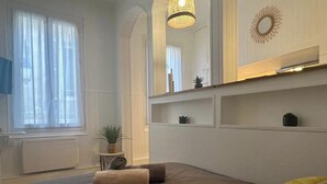 A bedroom with a large bed, a bedside table with a plant, a mirror above the bed, and a window with curtains. - Casa Cloutiers #2 - Studio - Hyper Centre Brive (Brive-la-Gaillarde)