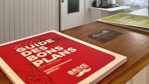 A room with a wooden desk, a red book titled "Guide to Global Plans," a green card, and a television on a stand. - Casa Cloutiers #2 - Studio - Hyper Centre Brive (Brive-la-Gaillarde)