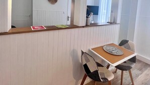 A dining area with a wooden table and chairs, white paneled walls, and a hanging light fixture. - Casa Cloutiers #2 - Studio - Hyper Centre Brive (Brive-la-Gaillarde)