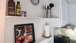 Una cocina con armarios blancos, un reloj, una tableta mostrando imágenes de comida y varios utensilios de cocina.