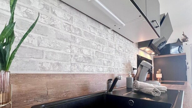 Eine moderne Küche mit einem schwarzen Spülbecken, einer Holzarbeitsplatte und einer Spritzschutzwand mit Ziegeloptik.