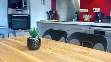 A modern kitchen with stainless steel appliances, a red accent wall, and a wooden dining table with a pineapple centerpiece.