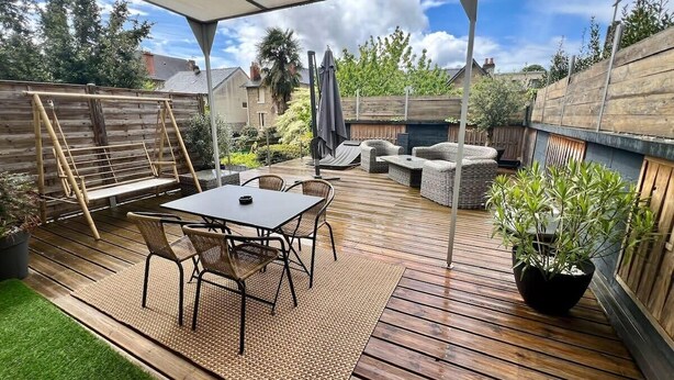 Eine Holzterrasse mit Tisch und Stühlen, einem Blumentopf und einem überdachten Sitzbereich.