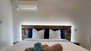 Ein ordentlich gemachtes Bett mit weißer und brauner Bettwäsche, einem Holz-Kopfteil und einer Deckenleuchte.