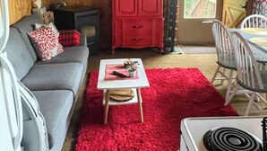 A cozy cabin interior with a grey sofa, a red cabinet, a small table with a plant, and a red rug. - Haven at Loon Lake (Grand Marais)
