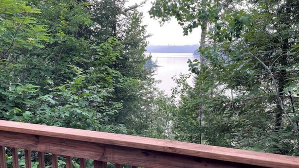 A wooden deck with a view of a lake surrounded by dense forest. - Haven at Loon Lake (Grand Marais)