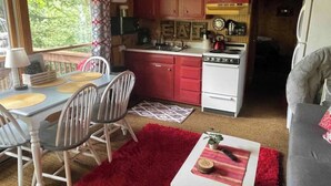 A compact kitchen with red cabinets, a white stove, and a dining area with a table and chairs. - Haven at Loon Lake (Grand Marais)