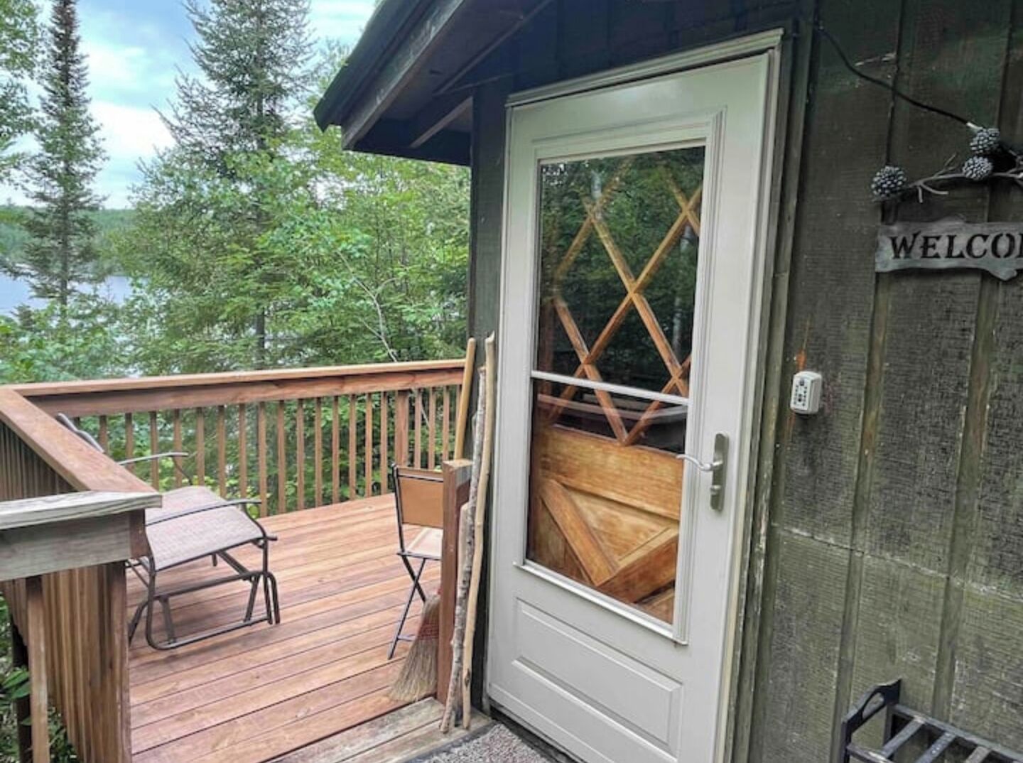A wooden deck with a bench and a folding table, a door with a glass panel, and a 'WELCOME' sign on the wall.