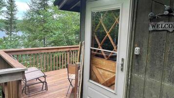 A wooden deck with a bench and a folding table, a door with a glass panel, and a 'WELCOME' sign on the wall.