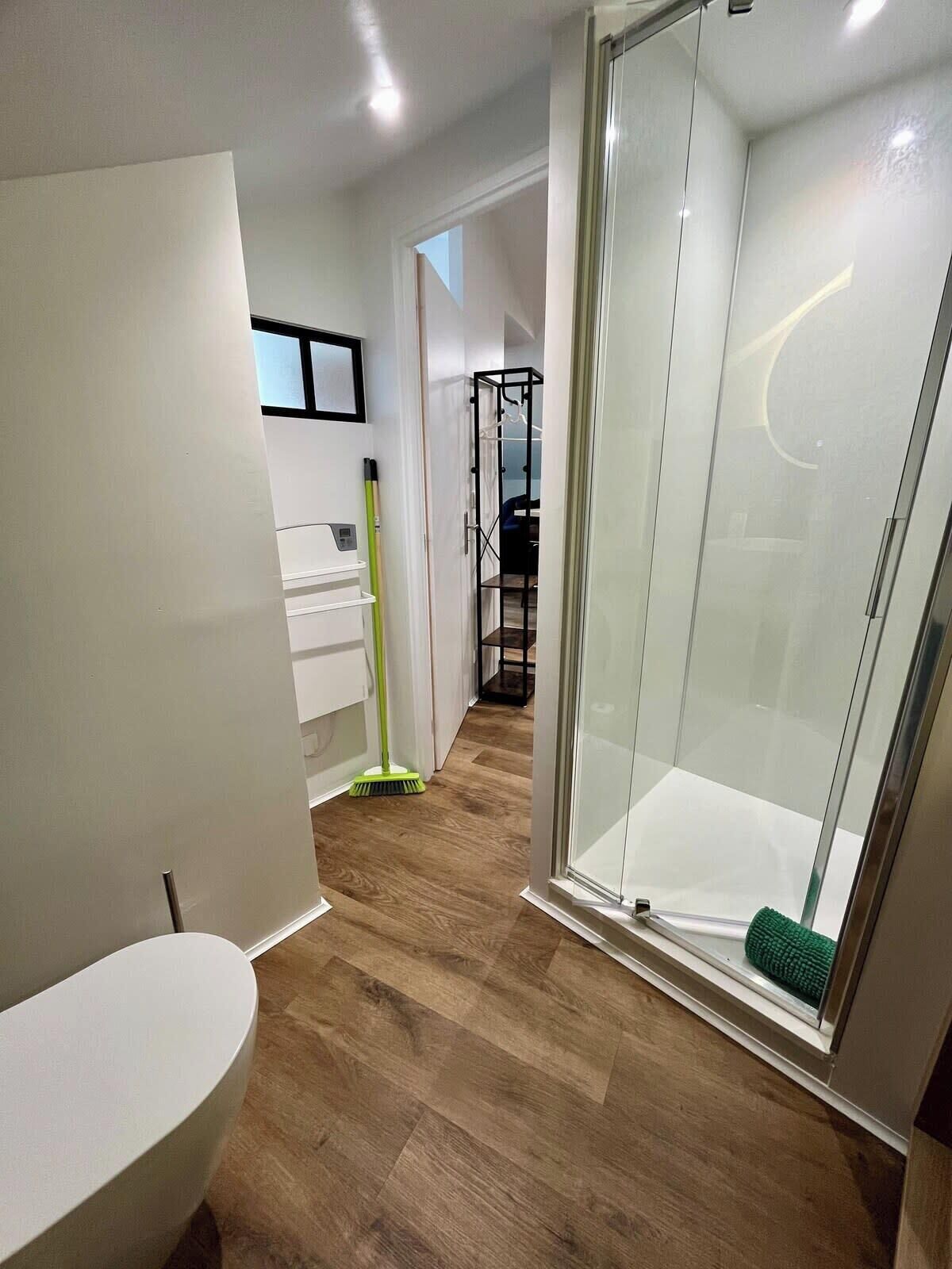 Ein modernes Badezimmer mit einer Duschkabine aus Glas, einem weißen Waschbecken und einem Holzboden.
