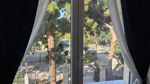 Vista a través de una ventana con cortinas, que muestra un parque con árboles, un parque infantil y una calle.