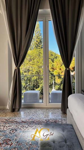Une chambre avec une grande fenêtre, un tapis à motifs et une tête de lit capitonnée.