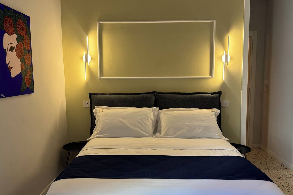 A neatly made bed with white and navy bedding, two bedside tables, and wall-mounted lights.