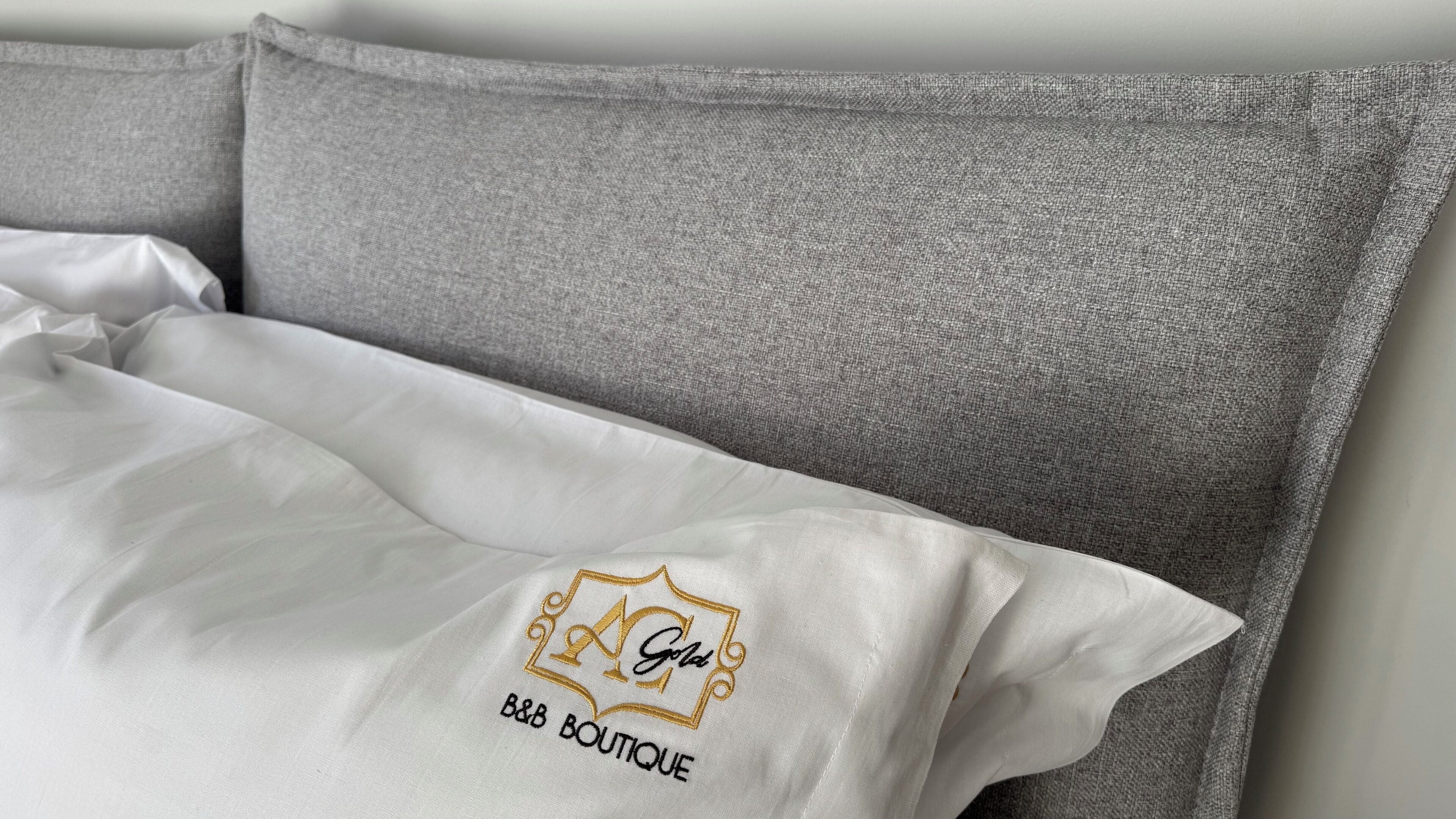 A bed with a white pillow and a grey pillow. The pillow has a logo and text that reads "B&B Boutique."