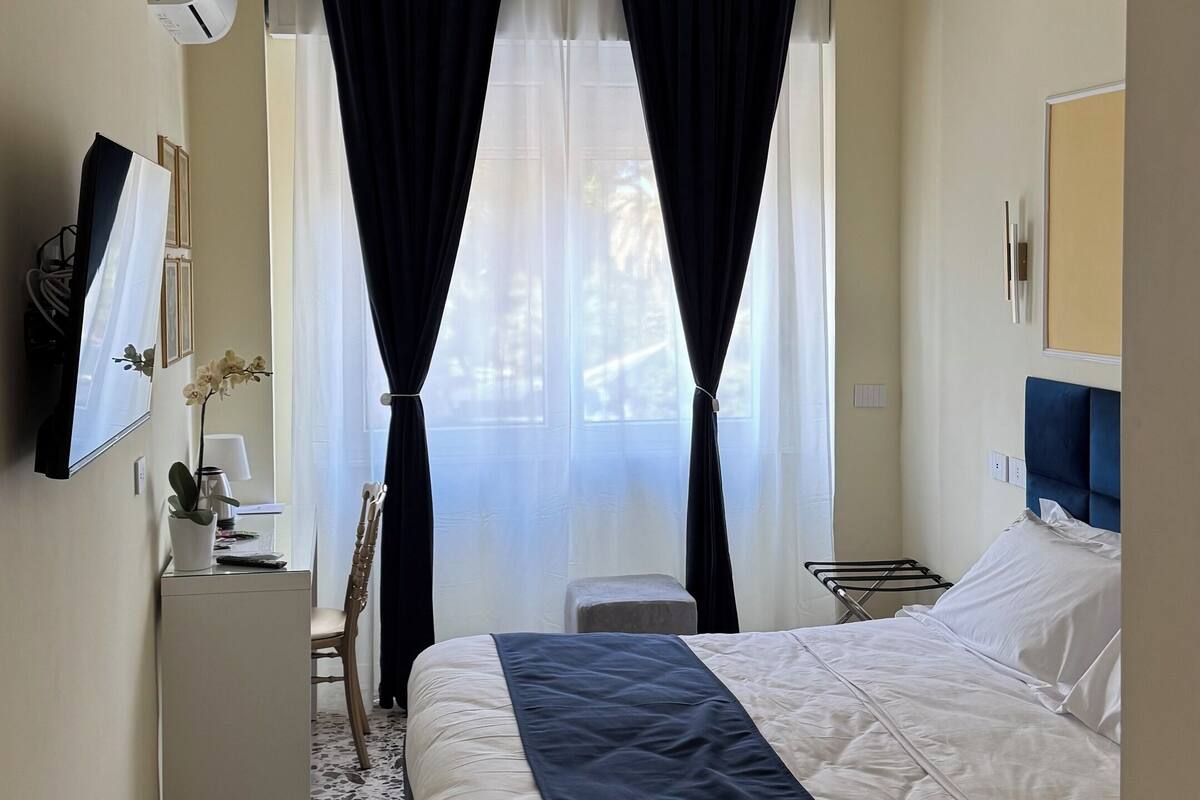 A hotel room with a bed, a desk, a chair, a small table, and a mirror.