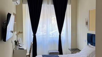 A hotel room with a bed, a desk, a chair, a small table, and a mirror.