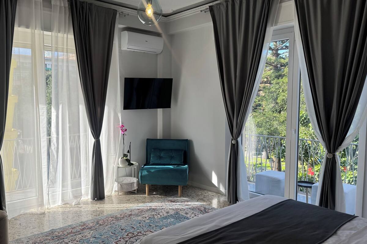 A modern hotel room with a large bed, a TV, and a balcony with a view of the outdoors.