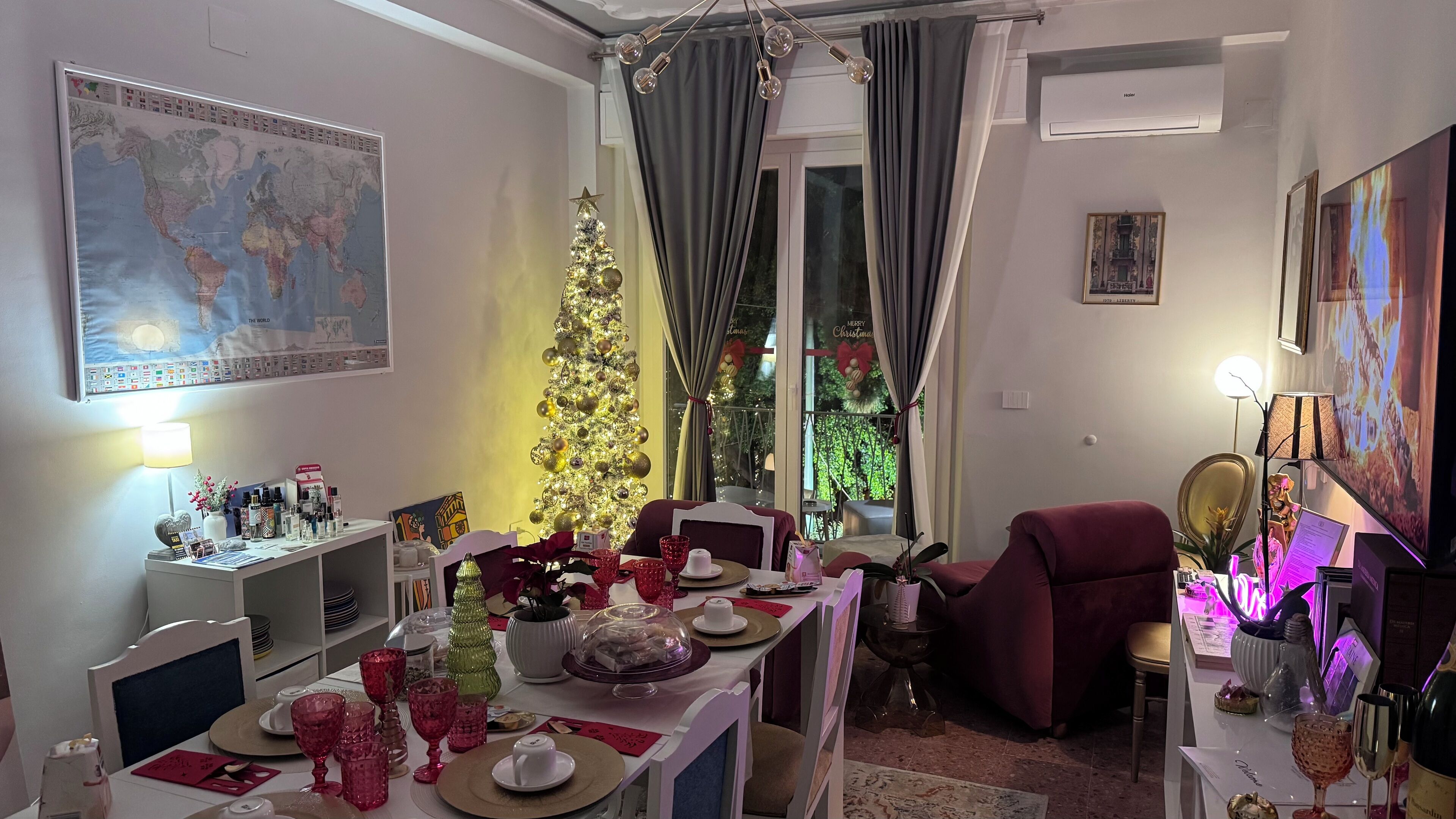 A dining area with a Christmas tree, a world map, and a large window with curtains.