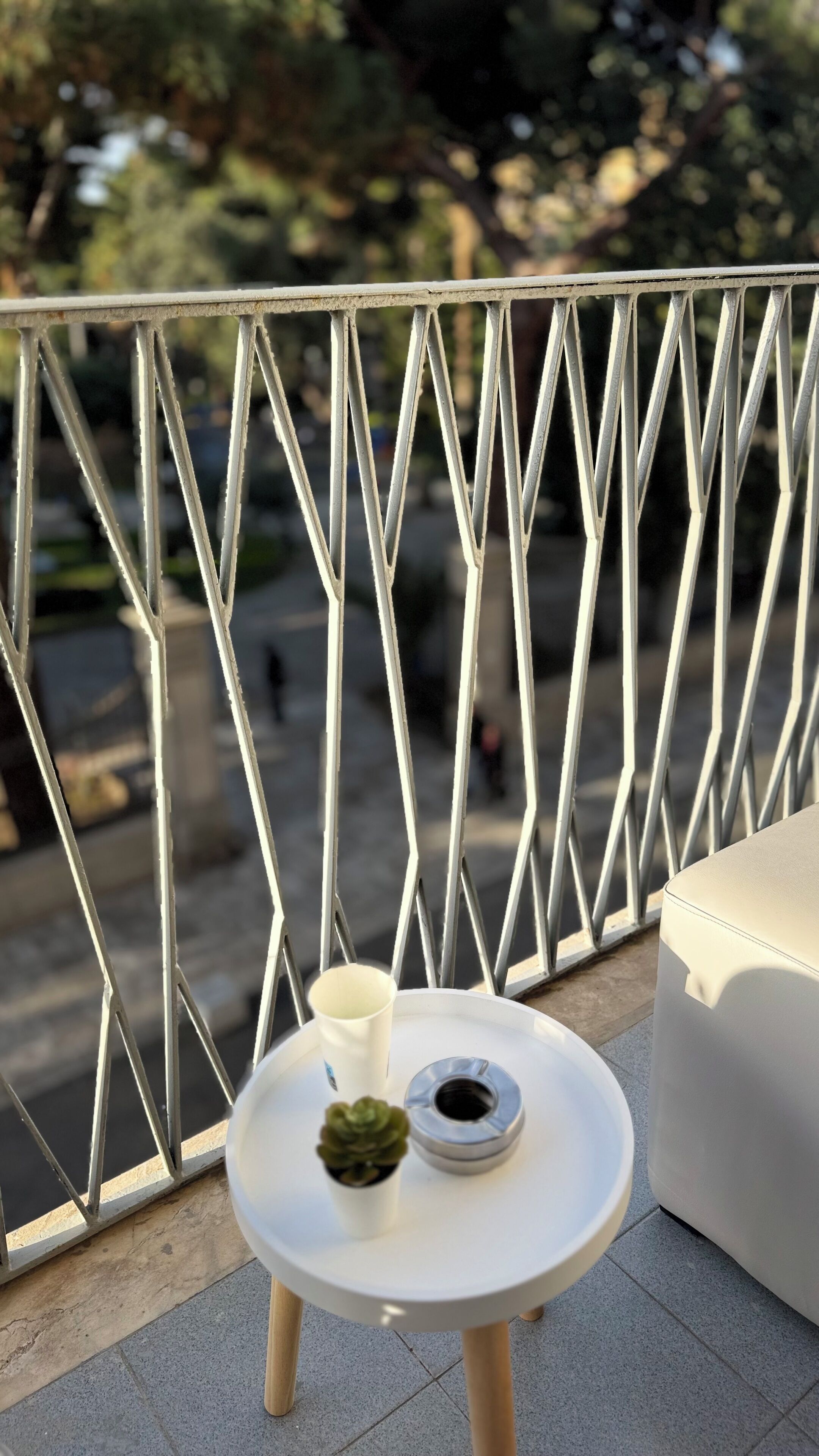 A small round table with a white cup, a small potted plant, and a metal object on a balcony with a metal railing.
