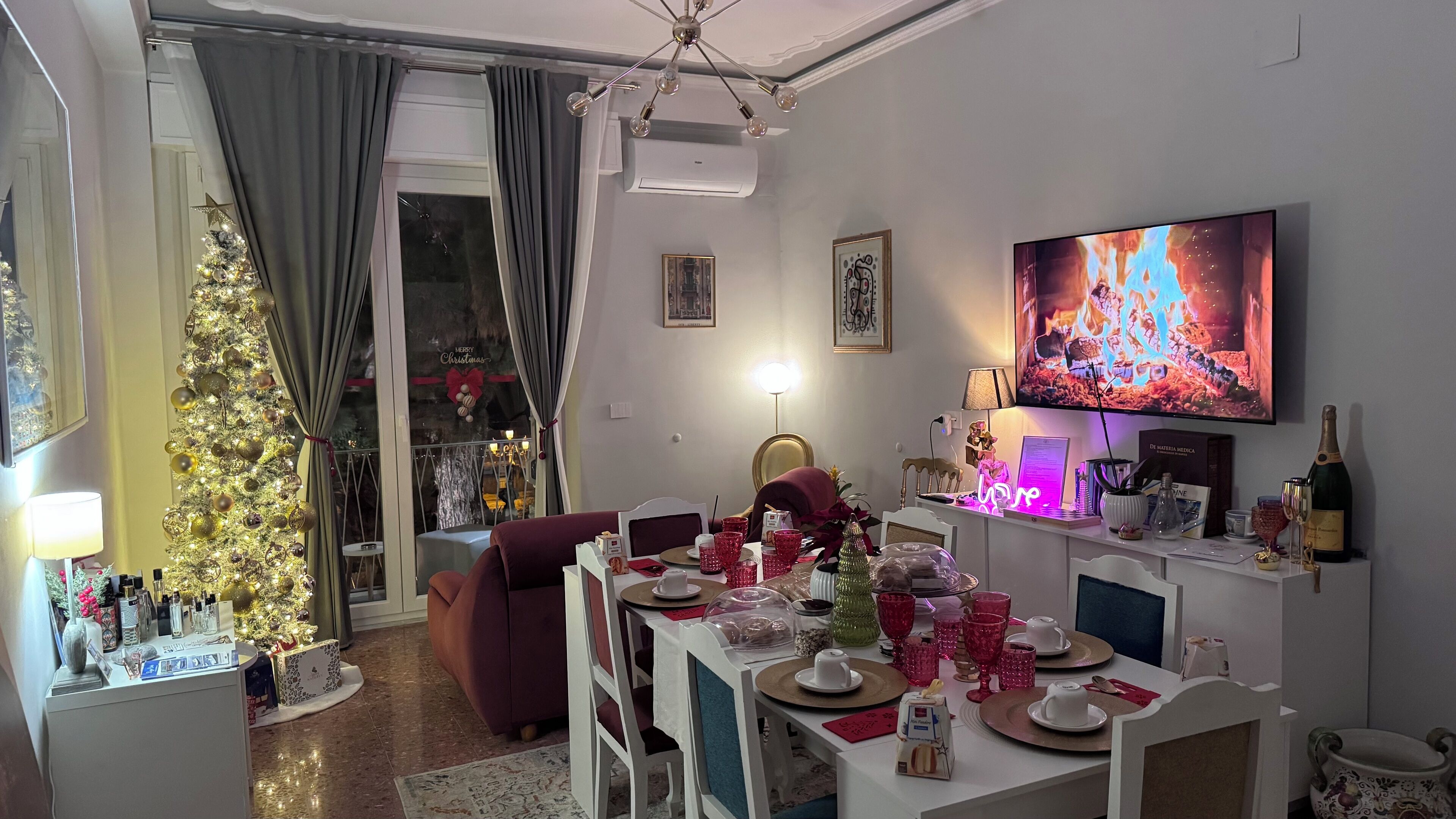 Uma sala de estar com uma árvore de Natal, uma mesa de jantar posta para quatro pessoas, uma televisão e uma garrafa de champanhe.