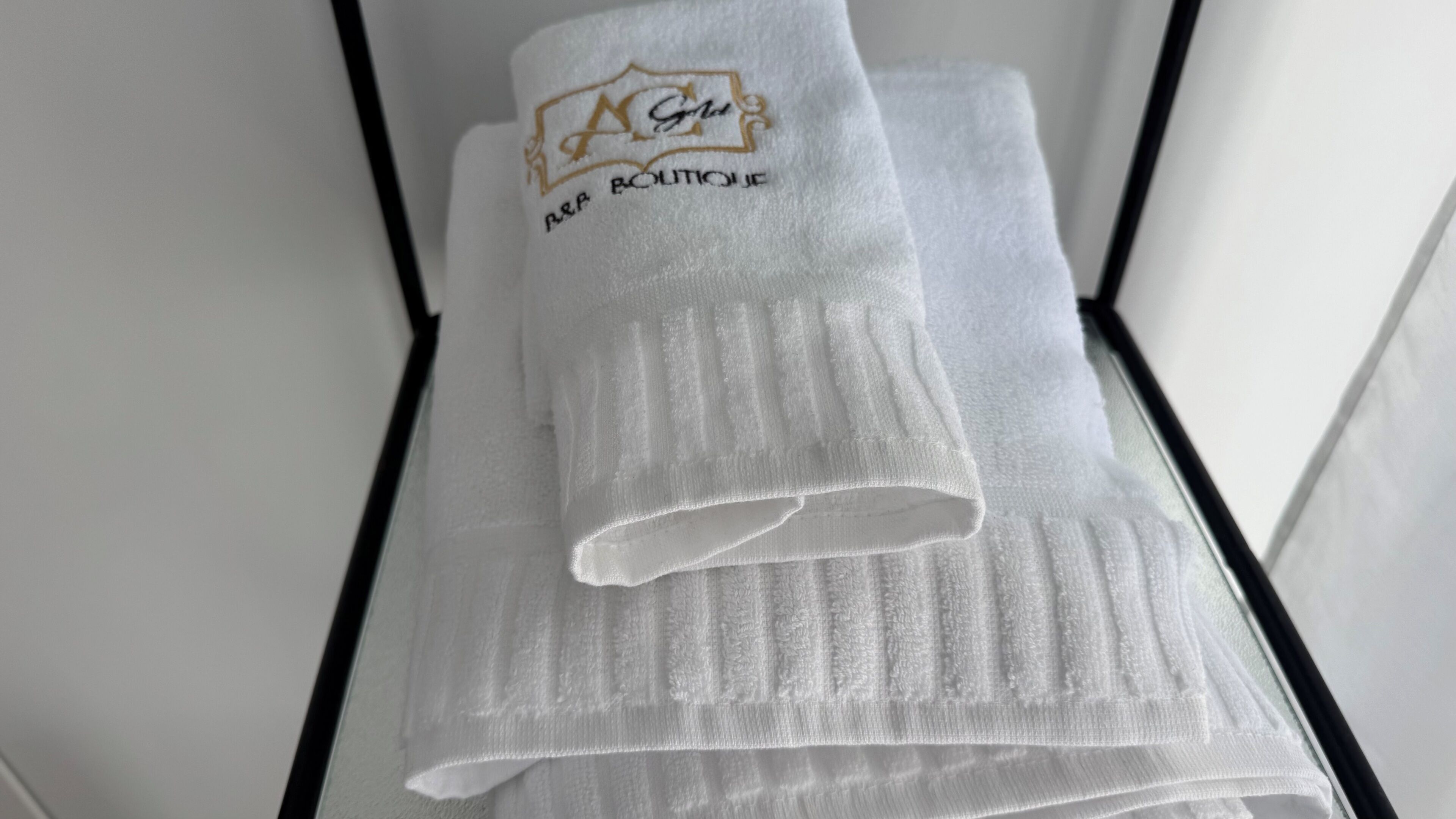 A neatly folded white towel with embroidered text and a logo, placed on a black surface.