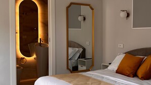 Un dormitorio moderno con cama, un espejo y un baño visible a través de un arco.