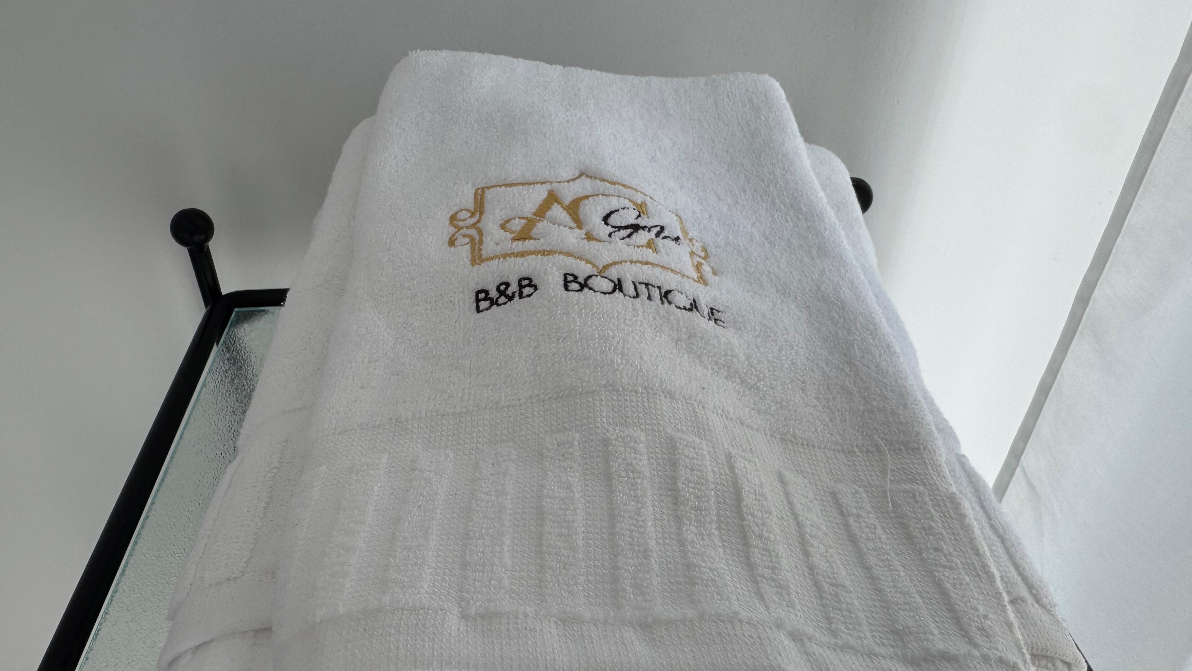 A white towel with embroidered text and logo on a wall-mounted rack.