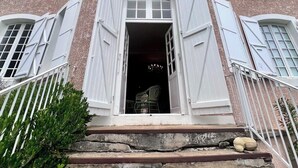 Ein mehrstöckiges Gebäude mit weißen Fensterläden, einer Steintreppe und einem Metallgeländer.