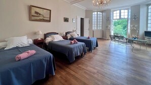 Ein Hotelzimmer mit drei Betten, einem Kronleuchter, einem großen Fenster und Blick auf Grün.