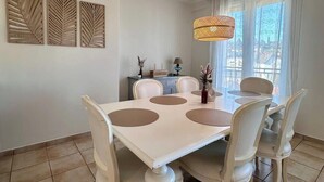 A dining area with a white table and chairs, a hanging light fixture, and a window with curtains. - Casa Ribot #10 - T4 pour 5 personnes - Proche Centre Ville (Brive-la-Gaillarde)