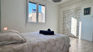 A bedroom with a bed, a window, a door, and a ceiling light. - Casa Ribot #10 - T4 pour 5 personnes - Proche Centre Ville (Brive-la-Gaillarde)