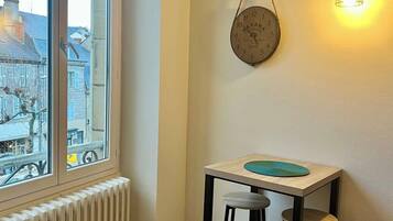 A room with a large window, a radiator, a table with stools, and a wall-mounted clock.