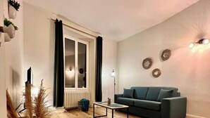 Een woonkamer met houten vloer, een bank, een salontafel en een raam met gordijnen.