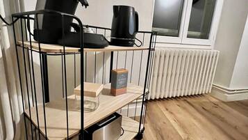 A kitchen area with a black coffee maker, a kettle, and a box of coffee on a black metal cart.