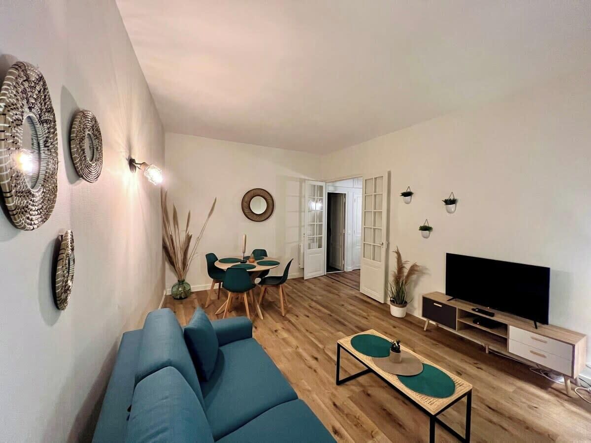 Een moderne woonkamer met een blauwe bank, een eettafel met stoelen, een tv-meubel en decoratieve wandkunst.