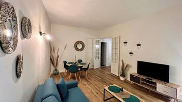 Een moderne woonkamer met een blauwe bank, een eettafel met stoelen, een tv-meubel en decoratieve wandkunst.