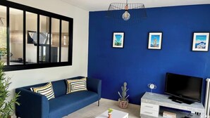 A modern living room with a blue sofa, white coffee table, and a TV on a grey entertainment unit.