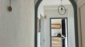 A hallway with a modern design, featuring a geometric wall clock, an arched doorway, and a hanging light fixture.