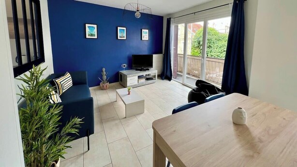 A modern living room with a blue accent wall, a flat-screen TV, a dining table, and a balcony with curtains.