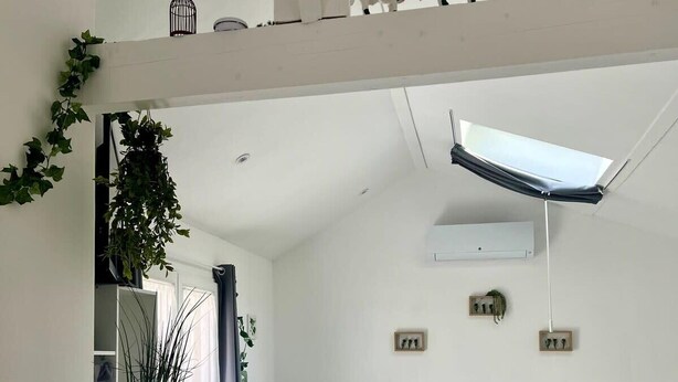 Una habitación moderna y luminosa con escritorio, silla y cama. Hay un tragaluz sobre la cama y una pequeña estantería con objetos decorativos.