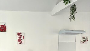 Una cocina moderna con encimera blanca, cafetera, fregadero y una pequeña isla con una cesta. Hay dos taburetes de bar y una silla.