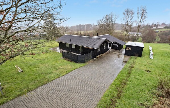 A rural property with a paved driveway leading to a wooden building with a sloped roof.