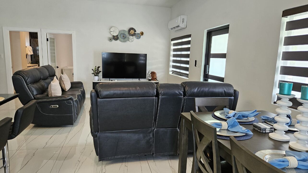Ein modernes Wohnzimmer mit einem schwarzen Ledersofa, einem Flachbildfernseher und einem Essbereich mit Tisch für zwei Personen.
