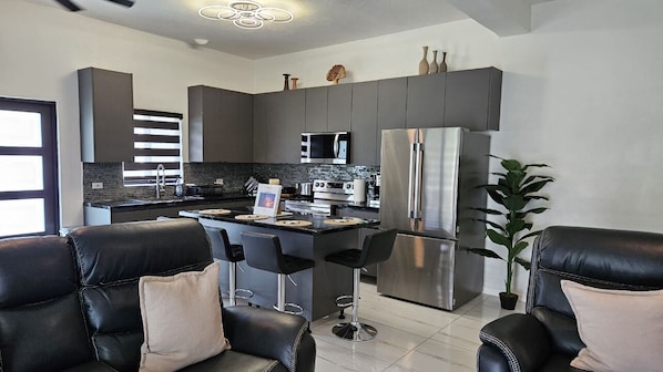 A modern kitchen with dark cabinetry, stainless steel appliances, and a central island with bar stools.