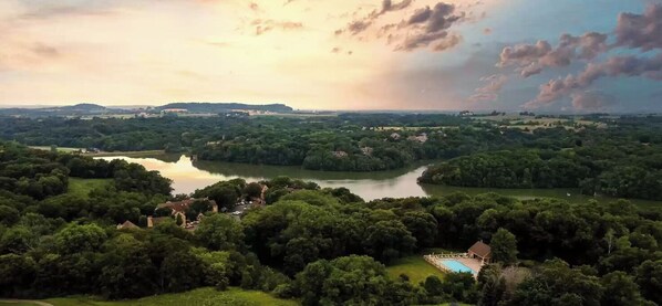 A lakeside property with a swimming pool, surrounded by dense greenery and a distant view of hills.