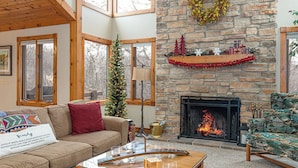 Un salon chaleureux avec une cheminée en pierre, un sapin de Noël et une étagère de cheminée décorée de cadeaux.